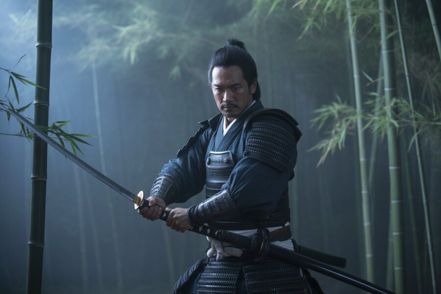 Guerreiro samurai Tomioka em armadura tradicional em uma floresta de bambu ao entardecer, segurando uma katana em posição de combate.